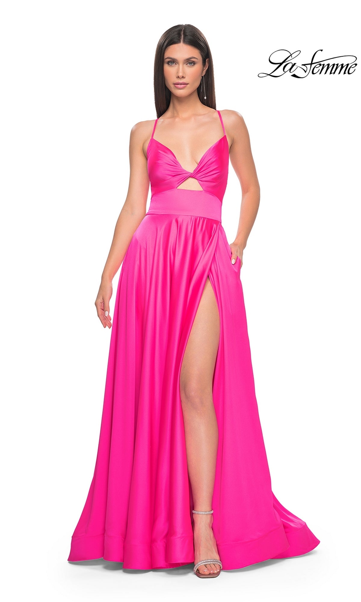 A woman models the La Femme Twist-Front Long A-Line Prom Dress 31412 in bright pink with a high slit and cutout detail, standing against a white background. The La Femme logo appears in the top right corner.